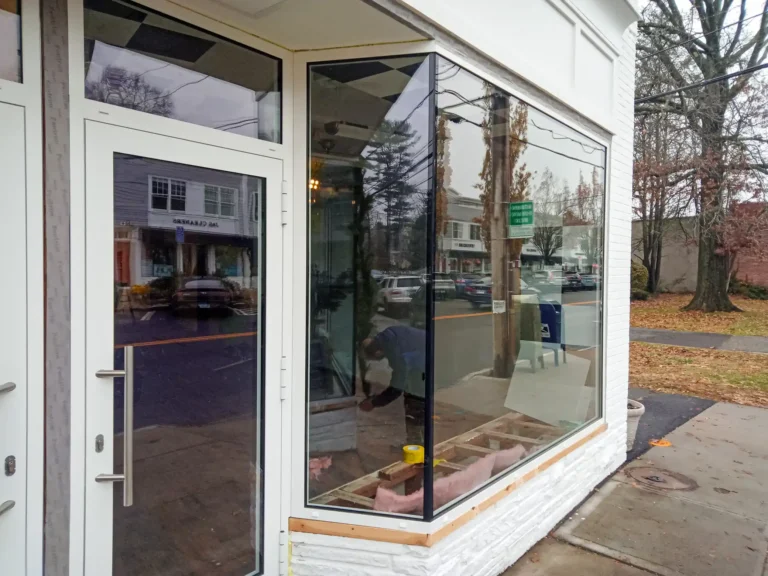 Glass window and doors of a white building storefront, reflecting the street scene.