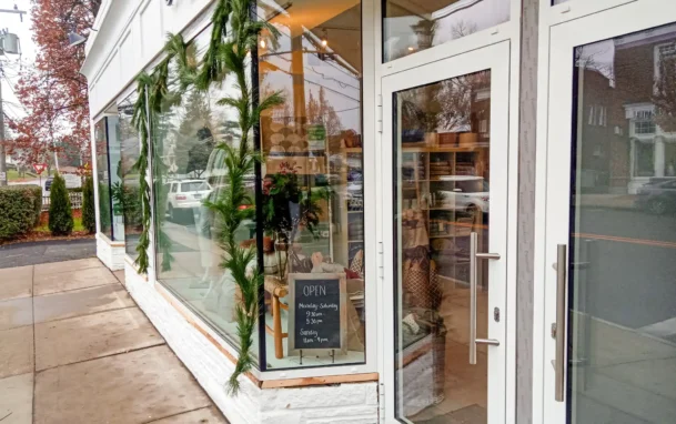 White building storefront with glass window and doors, greenery outside, and an 'open' sign displayed.