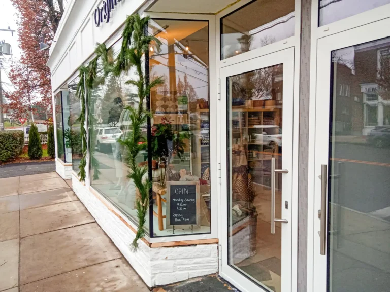 White building storefront with glass window and doors, greenery outside, and an 'open' sign displayed.